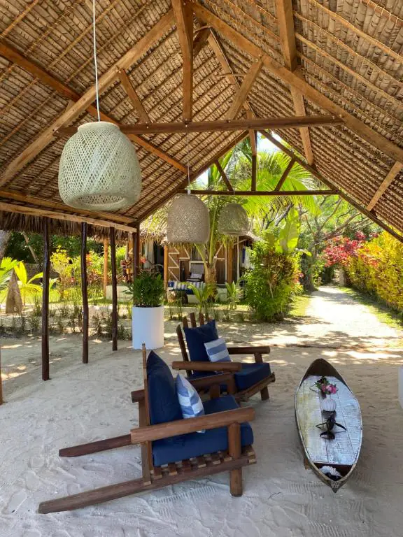 Vue depuis le salon vers l'allée de sable qui mène au bungalow, entre les massifs fleuris.