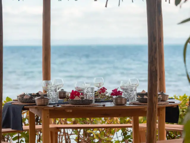 La table du dîner cadrée entre les poteaux de la paillote, l'océan calme derrière.